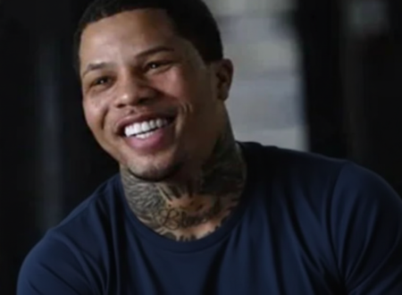 Smiling professional boxer with neck tattoos wearing a dark blue shirt, captured during an interview in an indoor setting.