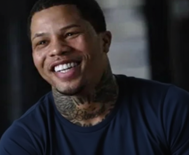 Smiling professional boxer with neck tattoos wearing a dark blue shirt, captured during an interview in an indoor setting.