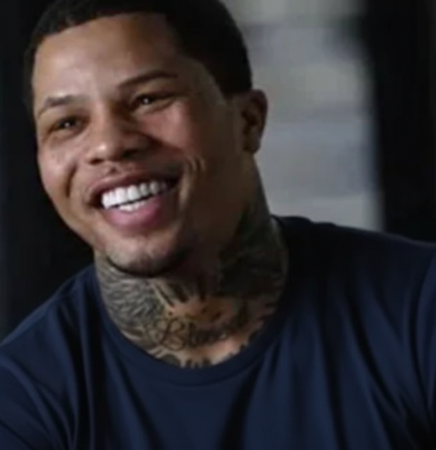 Smiling professional boxer with neck tattoos wearing a dark blue shirt, captured during an interview in an indoor setting.